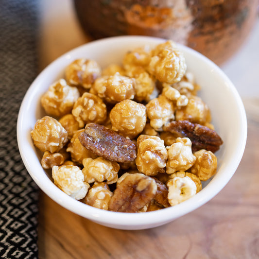 Ellis Bros Pecans caramel popcorn with pecan halves in white bowl on wooden board