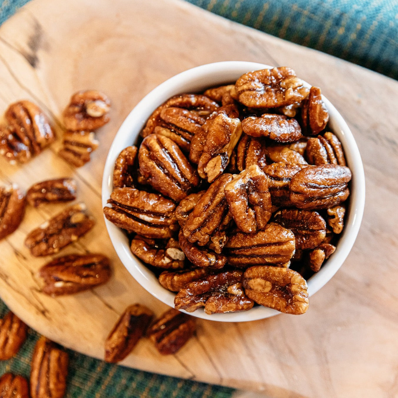 Candy coated pecan halves in white bowl on wooden board